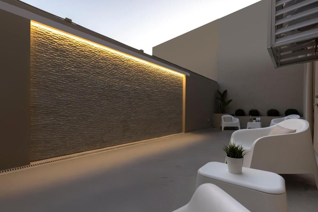 Lo spazio esterno di Sant’Elena Rooms al tramonto, con parete illuminata e poltrone bianche